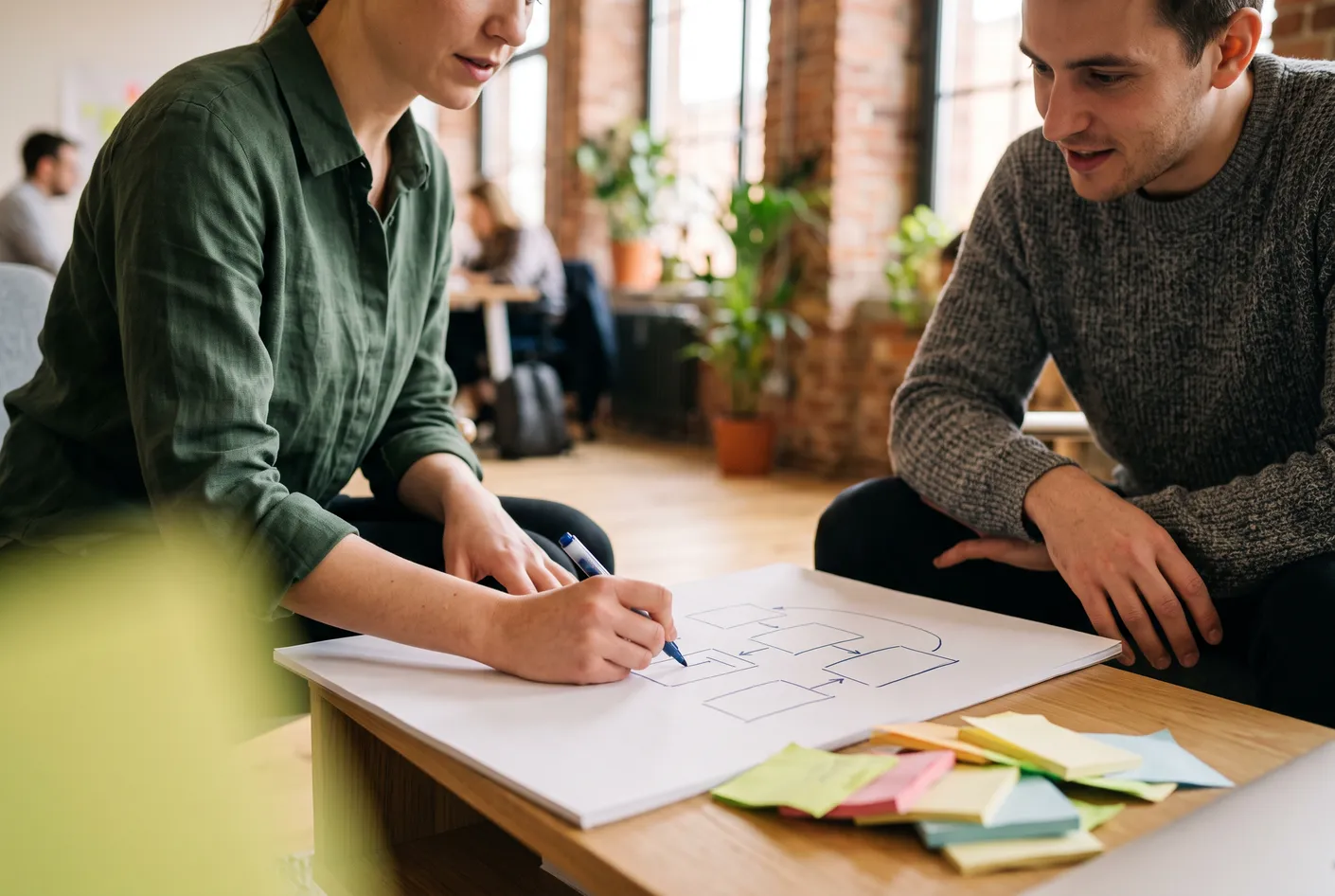 Two people in a coworking space sketching a simple plan with arrows on a large sheet of paper